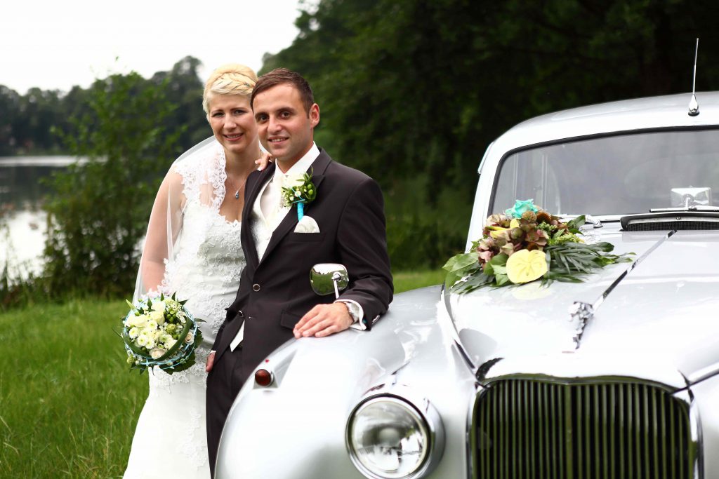 Brautpaar lehnt an Hochzeitsauto