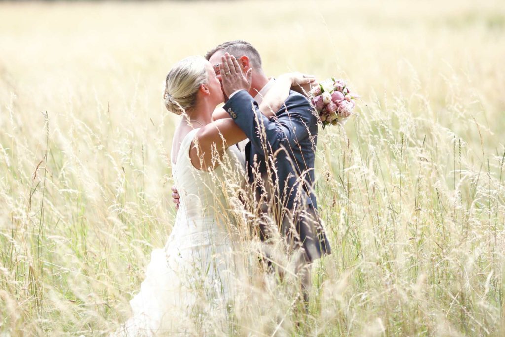 Hochzeitspaar im hohen Gras und Kuss